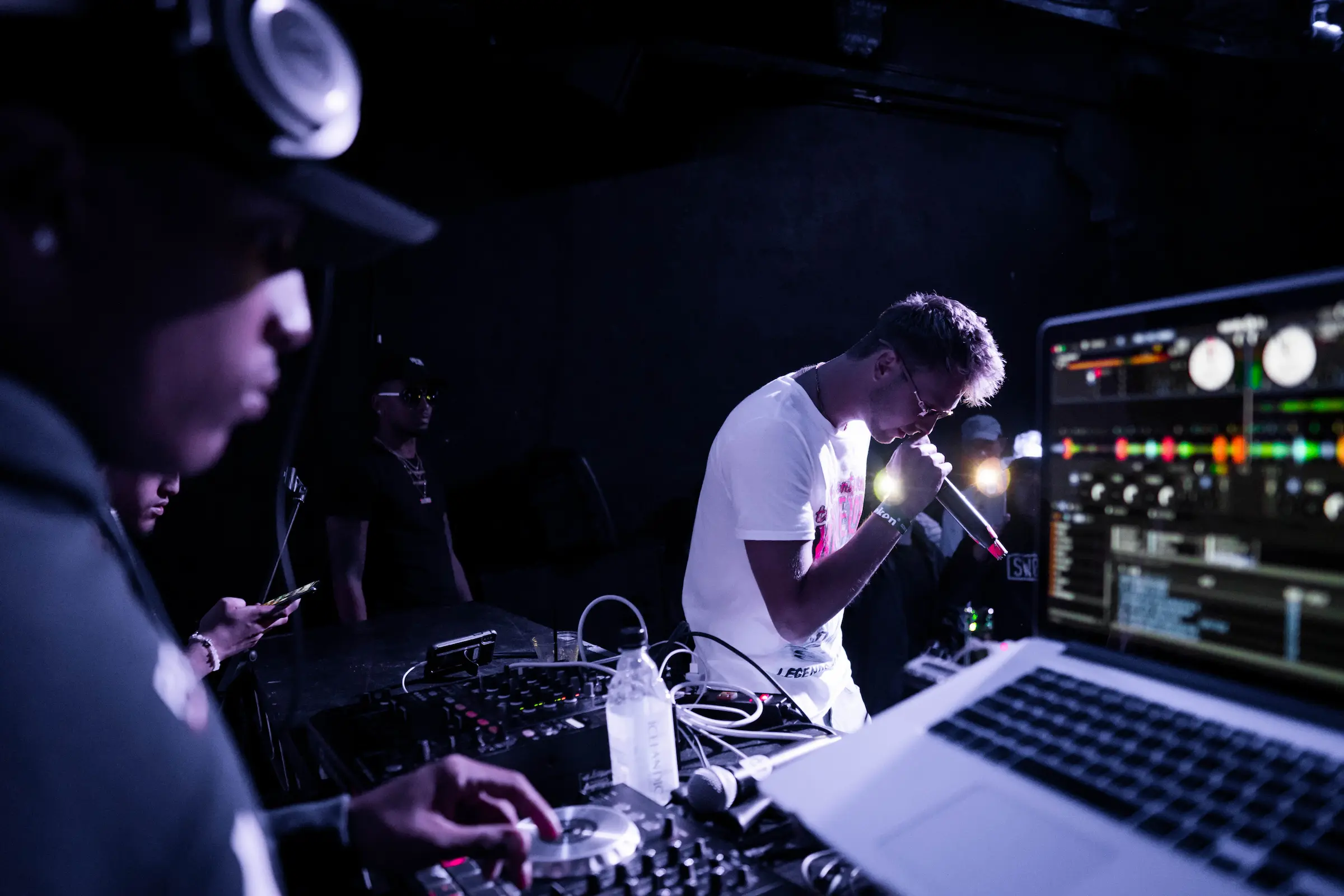 Backstage at a live show: artist on the mic over a DJ deck and laptop.